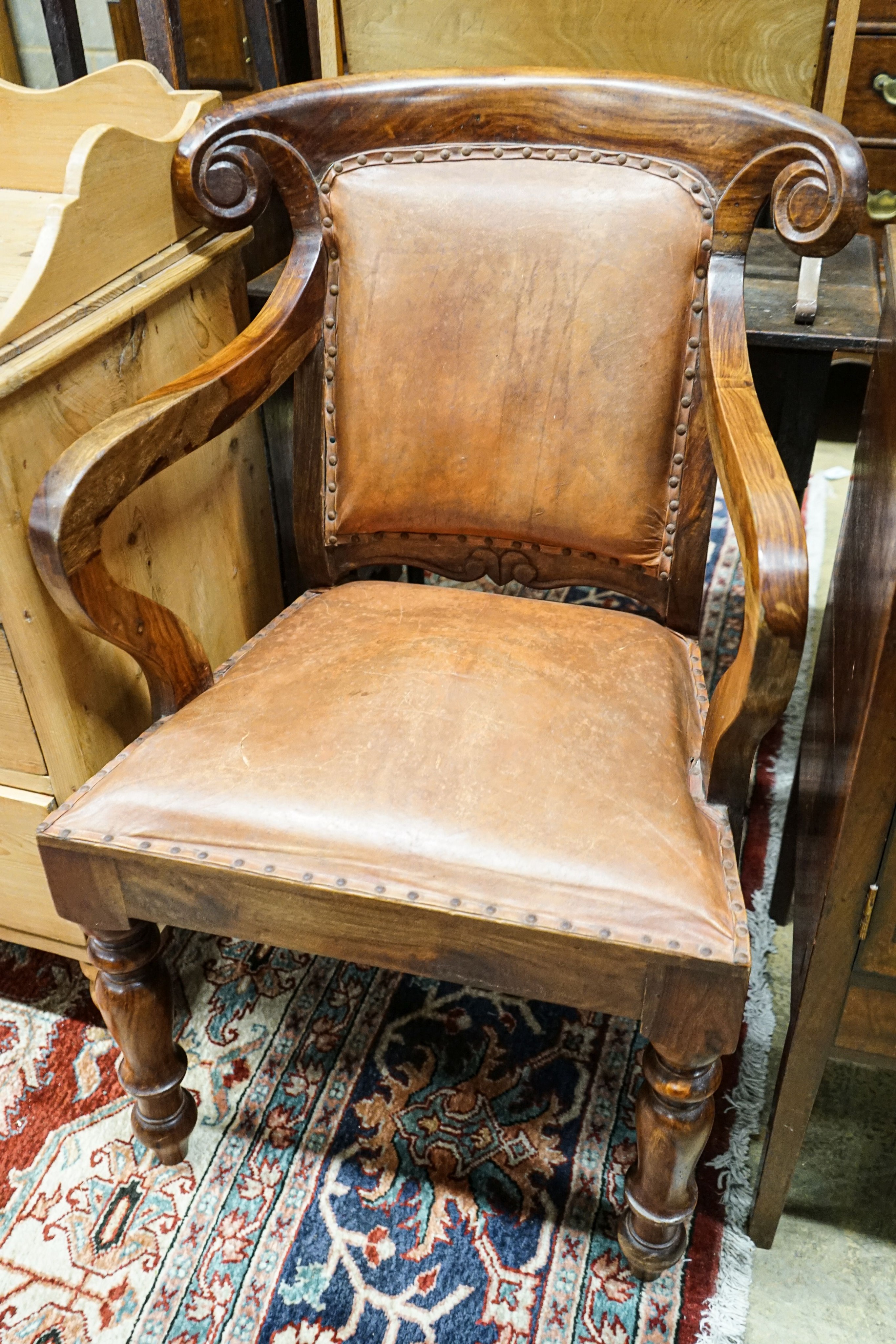 A pair of Victorian style hardwood elbow chairs with faded red leather upholstery, width 55cm, depth 45cm, height 92cm